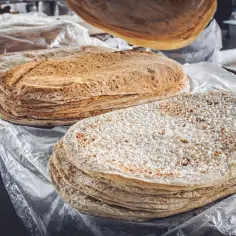 Stos cienkich, okrągłych placków, czyli lawaszu, leży na stole. Jeden placek jest podnoszony do góry.