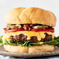 Soczysty burger wołowy z serem, pomidorem, ogórkiem i sałatą na talerzu.