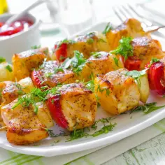 Szaszłyki z kurczaka z papryką i ziemniakami, pieczone w piekarniku, podane na talerzu z ziołami.