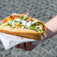 Kebab w bułce z warzywami i serem feta, trzymany w dłoni.