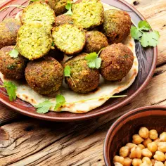 Talerz pełen chrupiących kulek, które są odpowiedzią na pytanie: co to jest falafel. Obok miseczka ciecierzycy, głównego składnika.