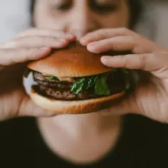 Osoba trzymająca w dłoniach soczystego burgera z podwójną wołowiną i sałatą.