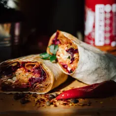 Dwa soczyste rolady efez doner kebab, pełne warzyw i mięsa, leżą obok czerwonej papryczki chili.
