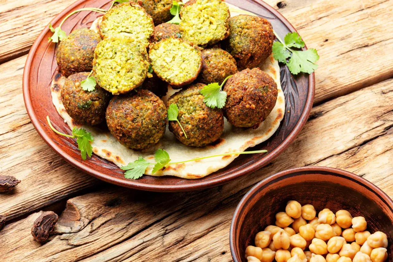 Talerz pełen chrupiących kulek, które są odpowiedzią na pytanie: co to jest falafel. Obok miseczka ciecierzycy, głównego składnika.