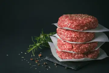 Stos surowych kotletów na burgery, idealne mięso na burgery, z gałązką rozmarynu i pieprzem w tle.