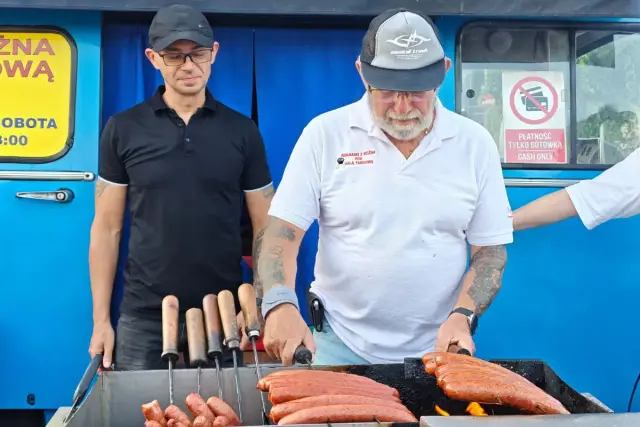 Smaczna kiełbasa z niebieskiej Nyski piecze się na grillu. Dwóch mężczyzn przygotowuje przysmak.